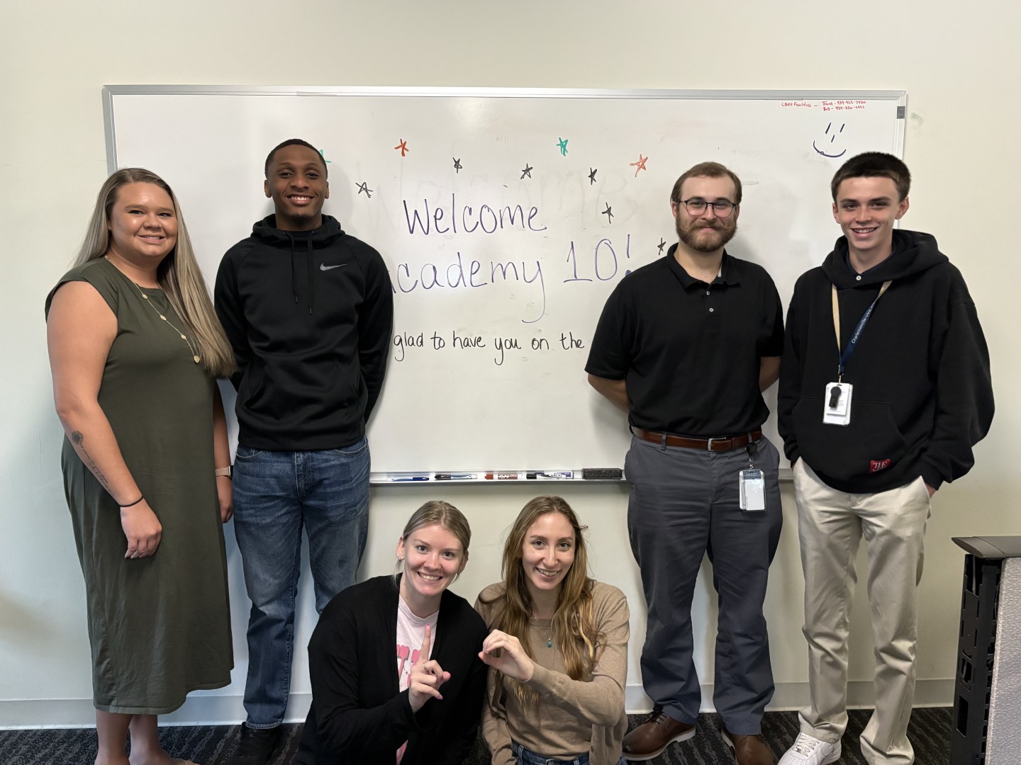 Five smiling people in front of a whiteboard that says "Welcome to Academy 10"